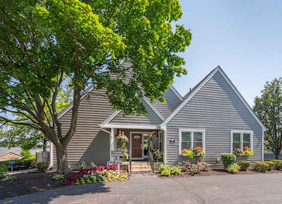A house with a grey siding and a brown door is surrounded by greenery.