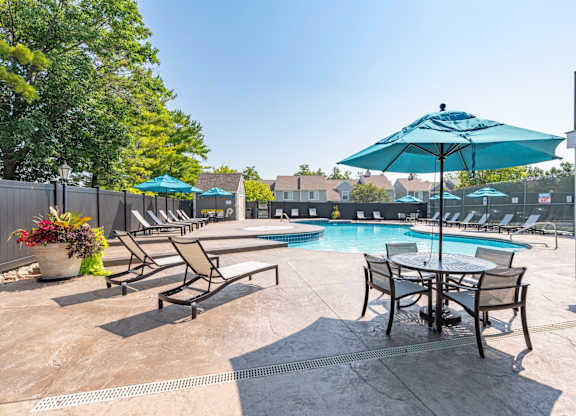 A poolside area with chairs, tables, and an umbrella.