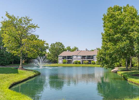 A house is surrounded by trees and a pond in front of it.