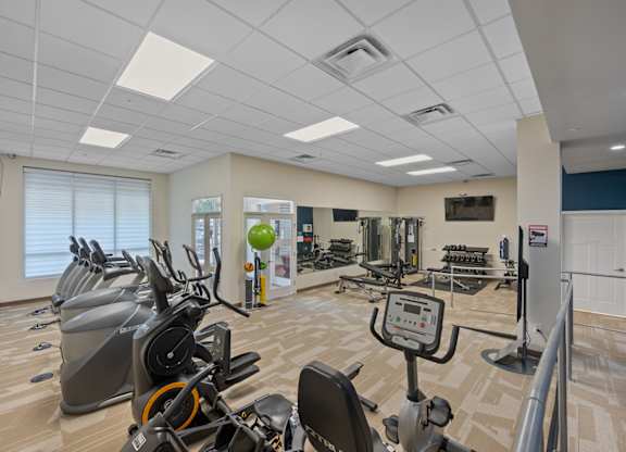 A gym with a variety of exercise equipment including treadmills, stationary bikes, and weight machines.