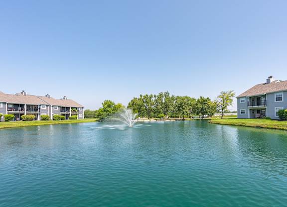 A fountain in the middle of a lake surrounded by houses.