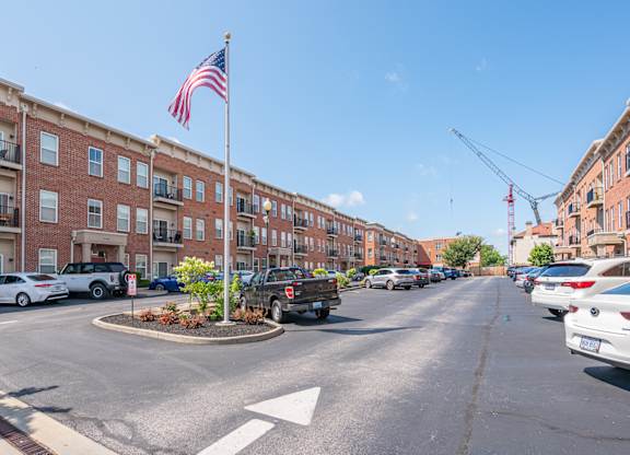 A street view with a flag on a pole and cars parked on the side.