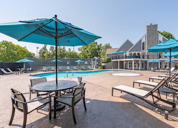 A poolside area with a table and chairs under a blue umbrella.