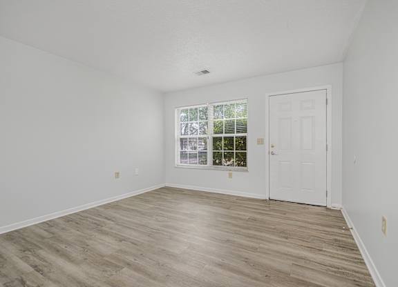 A room with a white door and a window with a view of trees.