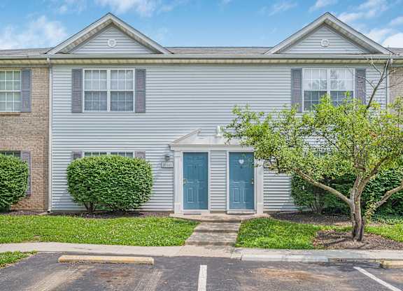 A grey house with a blue door and a tree in front.