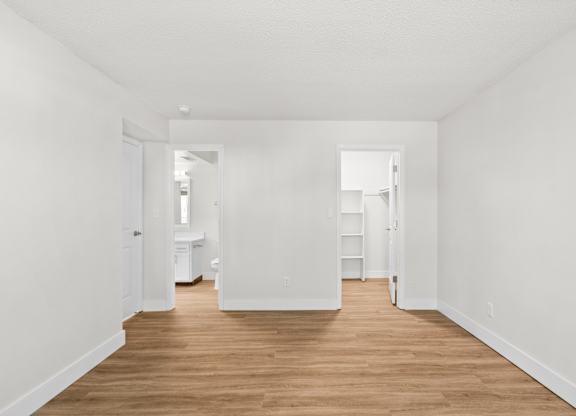 A long, narrow, white hallway with wood floors and white walls.