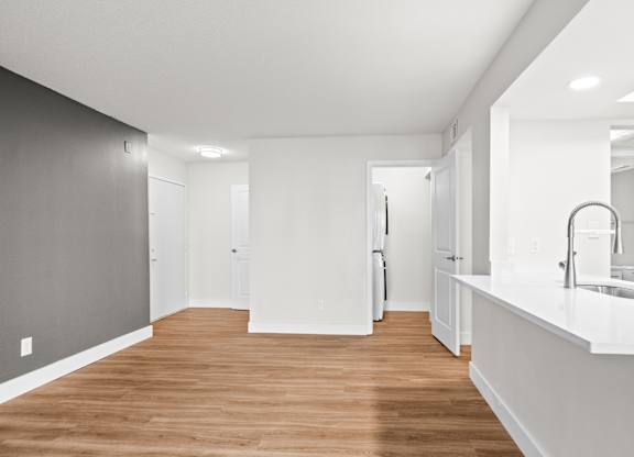 A long, narrow, white hallway with wood floors and white walls.