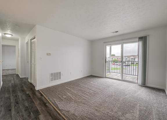 an empty living room with a sliding glass door to a balcony