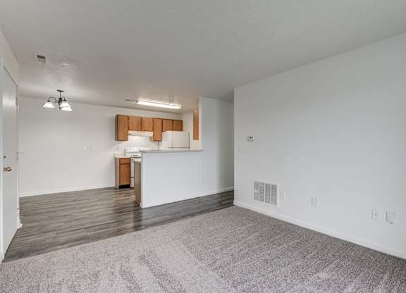an empty living room and kitchen with white walls and wood flooring