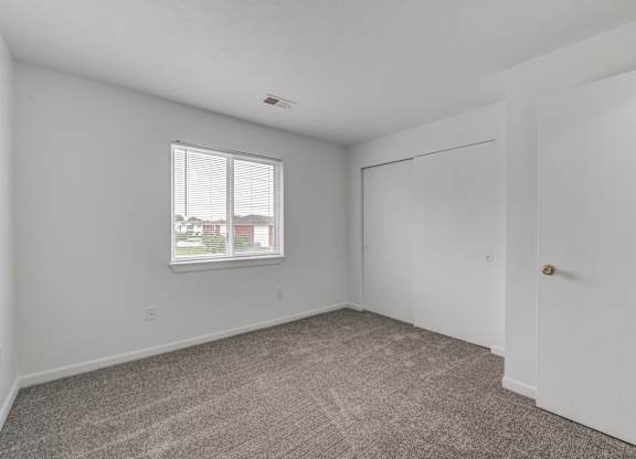 the living room of an apartment with carpet and a window