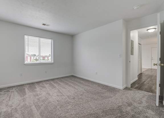 the living room of an apartment with carpet and a window