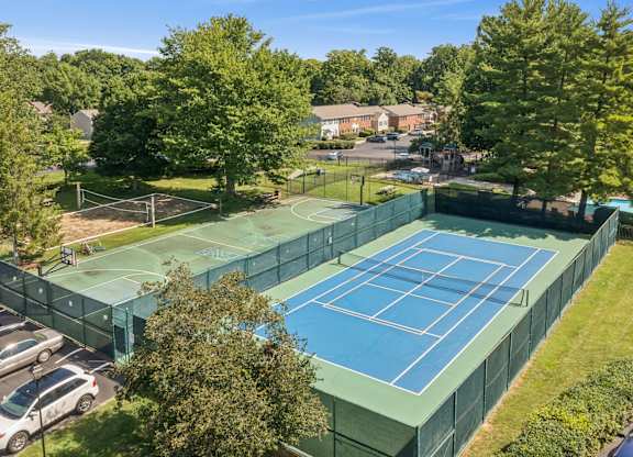 A tennis court surrounded by a green fence and trees.