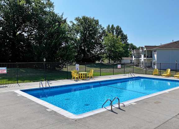A swimming pool surrounded by yellow chairs and a fence.