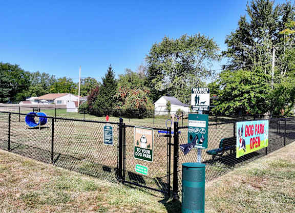A sign in front of a fence advertises a dog park.