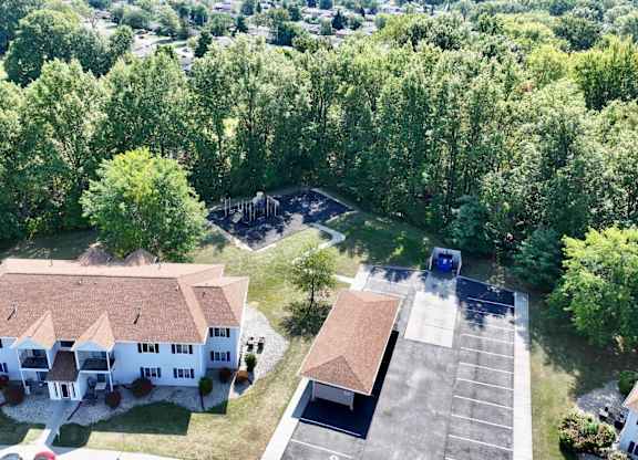 A large white house with a brown roof is surrounded by a parking lot and trees.