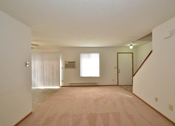 A room with a carpeted floor and a staircase on the right side.
