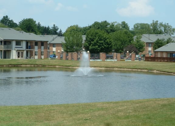 a fountain in the middle of a pond in front of an apartment building