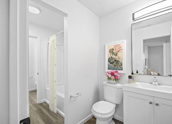 A white bathroom with a toilet, sink, and a painting of flowers.