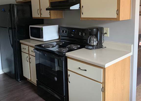A kitchen with a black refrigerator, white oven, and wooden cabinets.