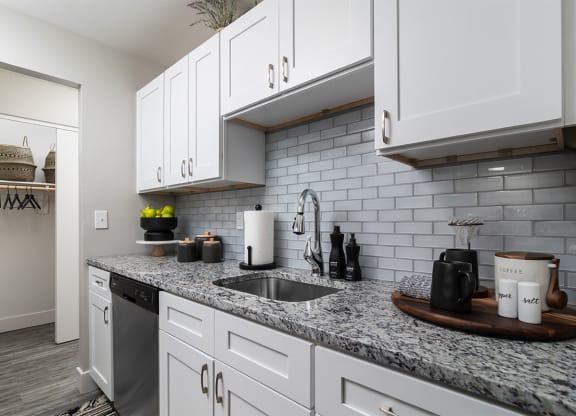 a white kitchen with marble counter tops and white cabinets at The Heights Apartments, Ohio