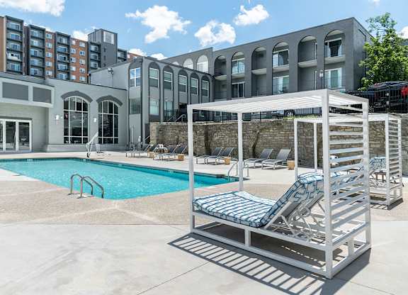 a pool with a chaise lounge chair in front of a building at The Heights Apartments, Cincinnati