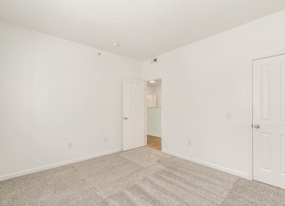 a bedroom with white walls and carpet and a door to a closet