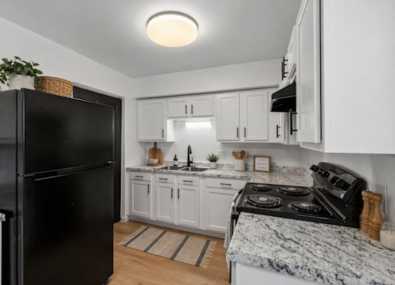 A black fridge stands in a kitchen with white cabinets and a marble countertop.