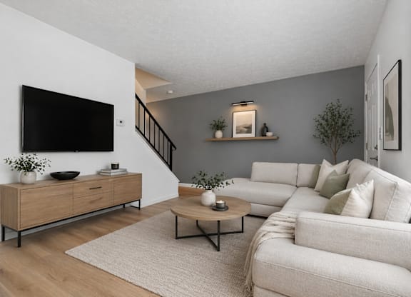 A living room with a white couch, a wooden cabinet, and a flat-screen TV mounted on the wall.