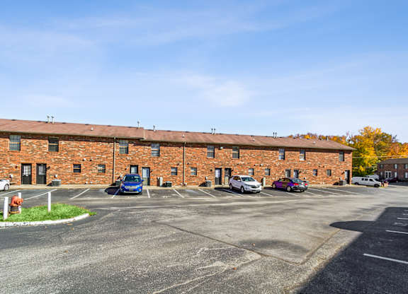 A parking lot in front of a brick building with cars parked.
