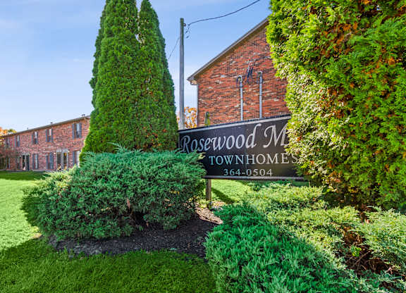 A sign for Rosewood Manor Townhomes stands in front of a brick building.