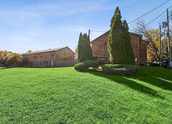 A green lawn in front of a brick building with trees.