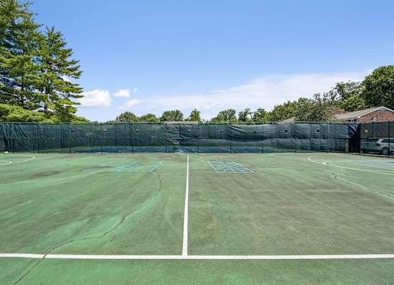 A tennis court with a green fence and trees in the background.