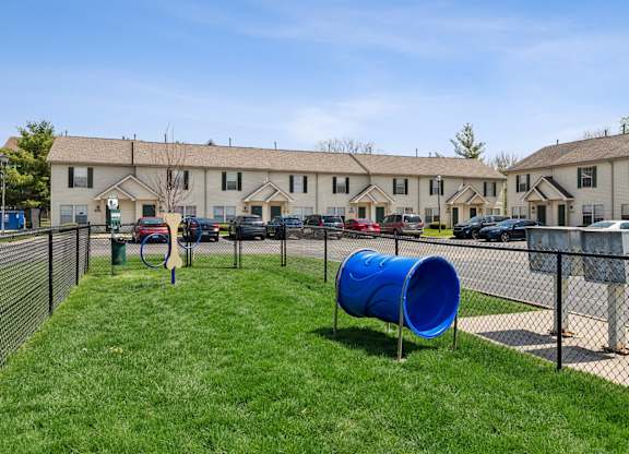 A blue barrel is in the grass in front of a chain link fence.