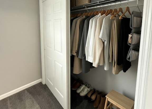 A white closet with clothes hanging and a bench underneath.