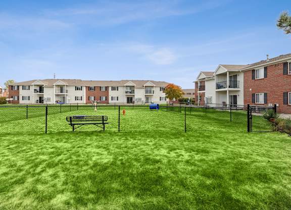 A grassy area with a bench and a fence in front of apartment buildings.