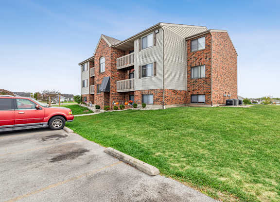 A red car is parked in a parking lot in front of a brick apartment building.