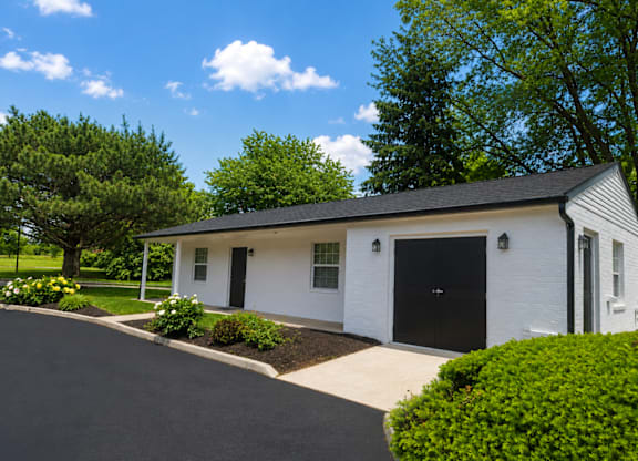 A white house with a black door and windows is surrounded by greenery.