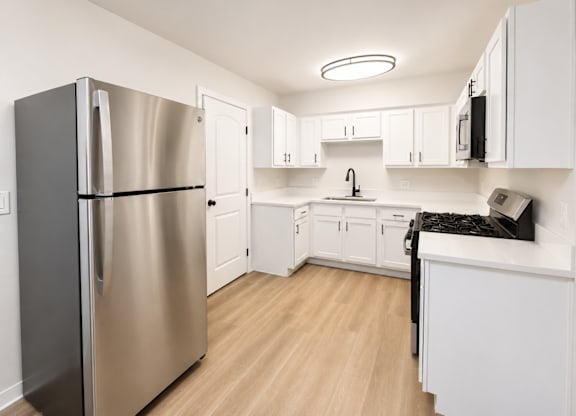 A kitchen with a refrigerator, cabinets, and a counter.