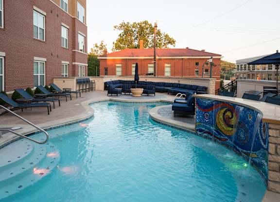 A swimming pool surrounded by lounge chairs and a brick building.