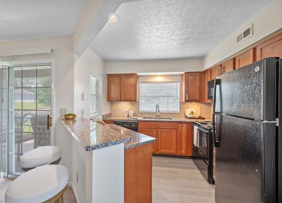 A kitchen with a black refrigerator and wooden cabinets.