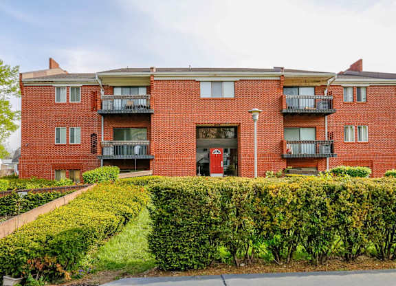 A red brick apartment building with a green hedge in front.