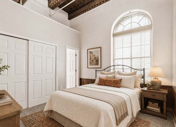 A bedroom with a large bed, a nightstand, and a window.