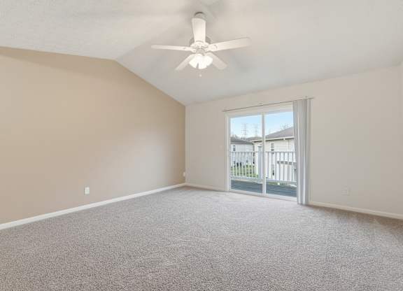 A room with a ceiling fan and a sliding glass door leading to a balcony.