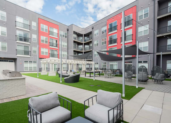an outdoor area with chairs and a lawn in front of an apartment building