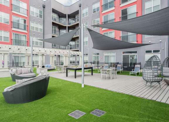 an outdoor lounge area with chairs and umbrellas in front of an apartment building