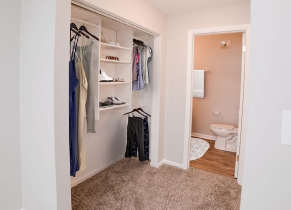 A white closet with clothes hanging and a toilet in the background at The Alpine Apartments, Kettering, OH, 45429