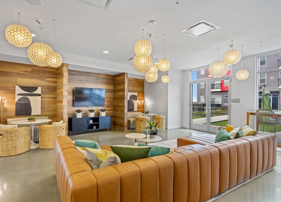 Apartments in Liberty Township, OH, with In-Unit Washer and Dryer - Liberty Center - Community Lounge with Leather Sectional Couch, Booth-Style Seating, Media Cabinet, Wall-Mounted TV, Glass Doors, and Floor-to-Ceiling Windows.