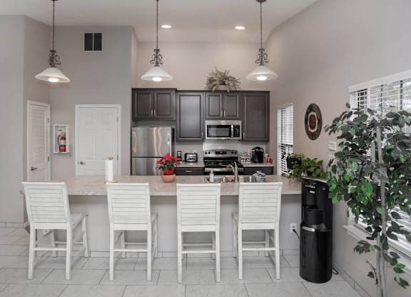 A kitchen with white chairs and a black trash can.