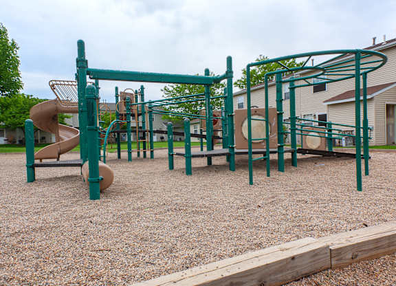 A playground with a green slide and monkey bars.