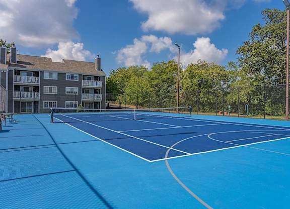 A blue tennis court is surrounded by trees and a building.